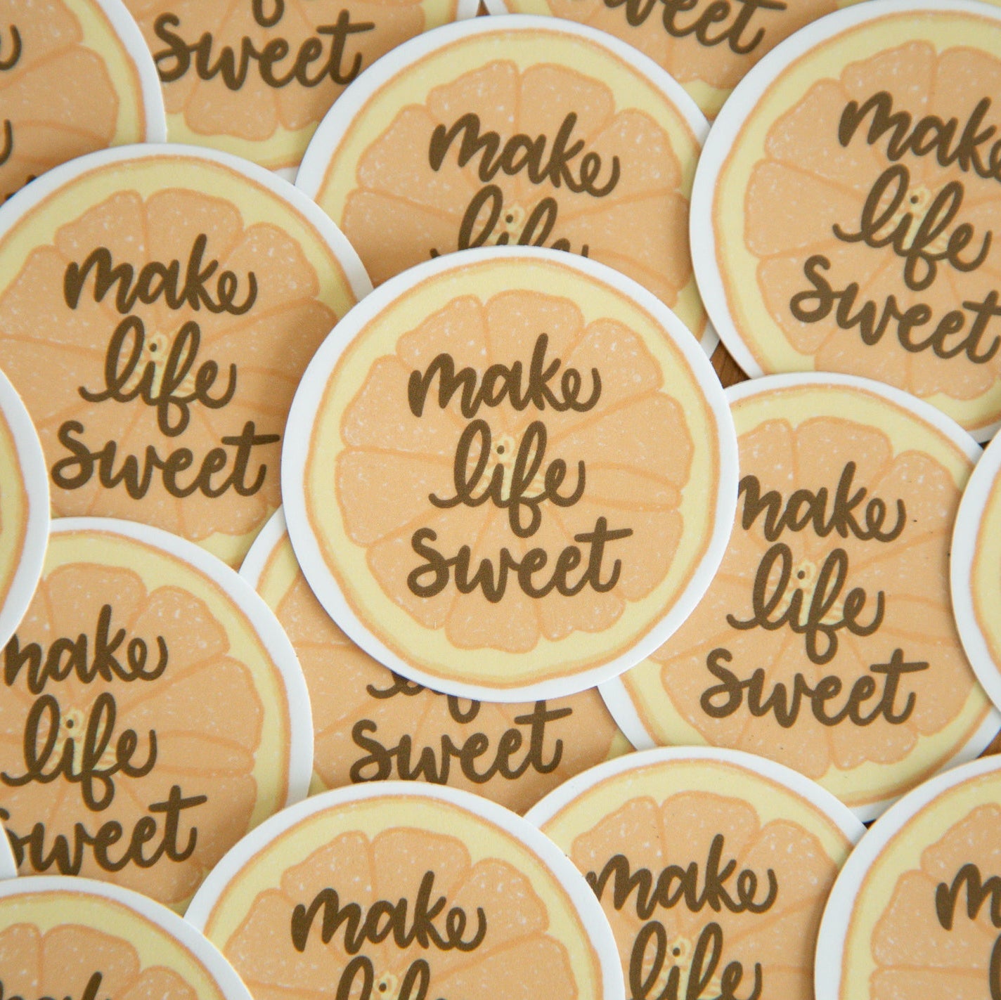 Multiple orange slice stickers with 'make life sweet' text on a wooden surface