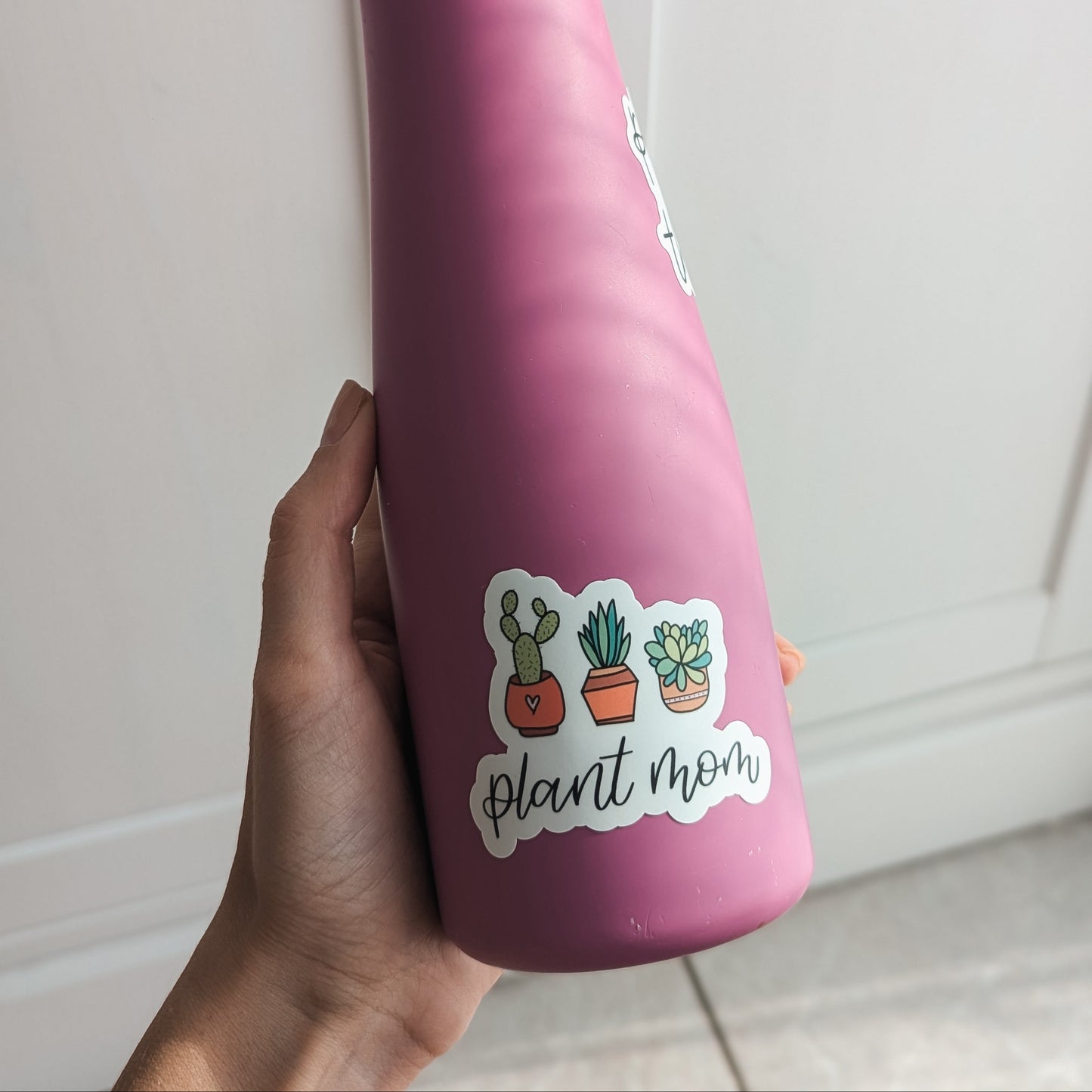 Hand holding a water bottle with vinyl sticker of 3 potted plants and the words "plant mom" in calligraphy underneath.