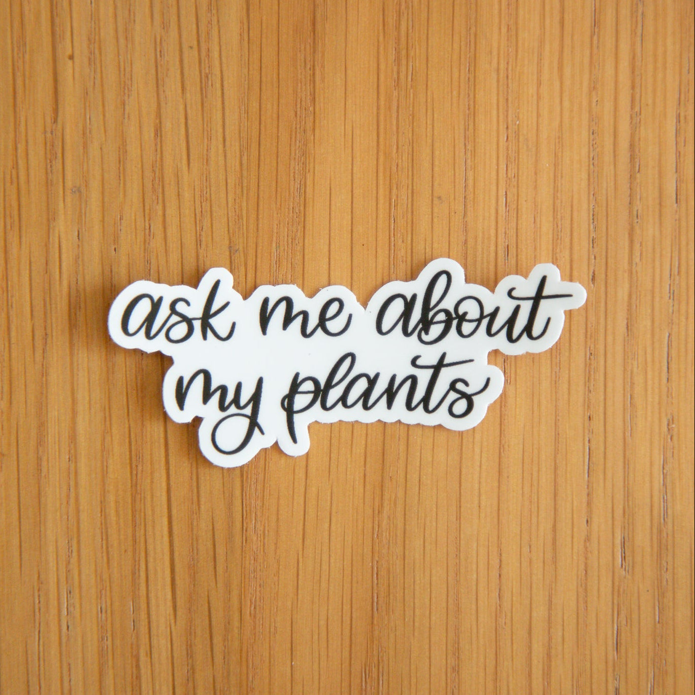 Black and white sticker with 'ask me about my plants' text on a wooden surface