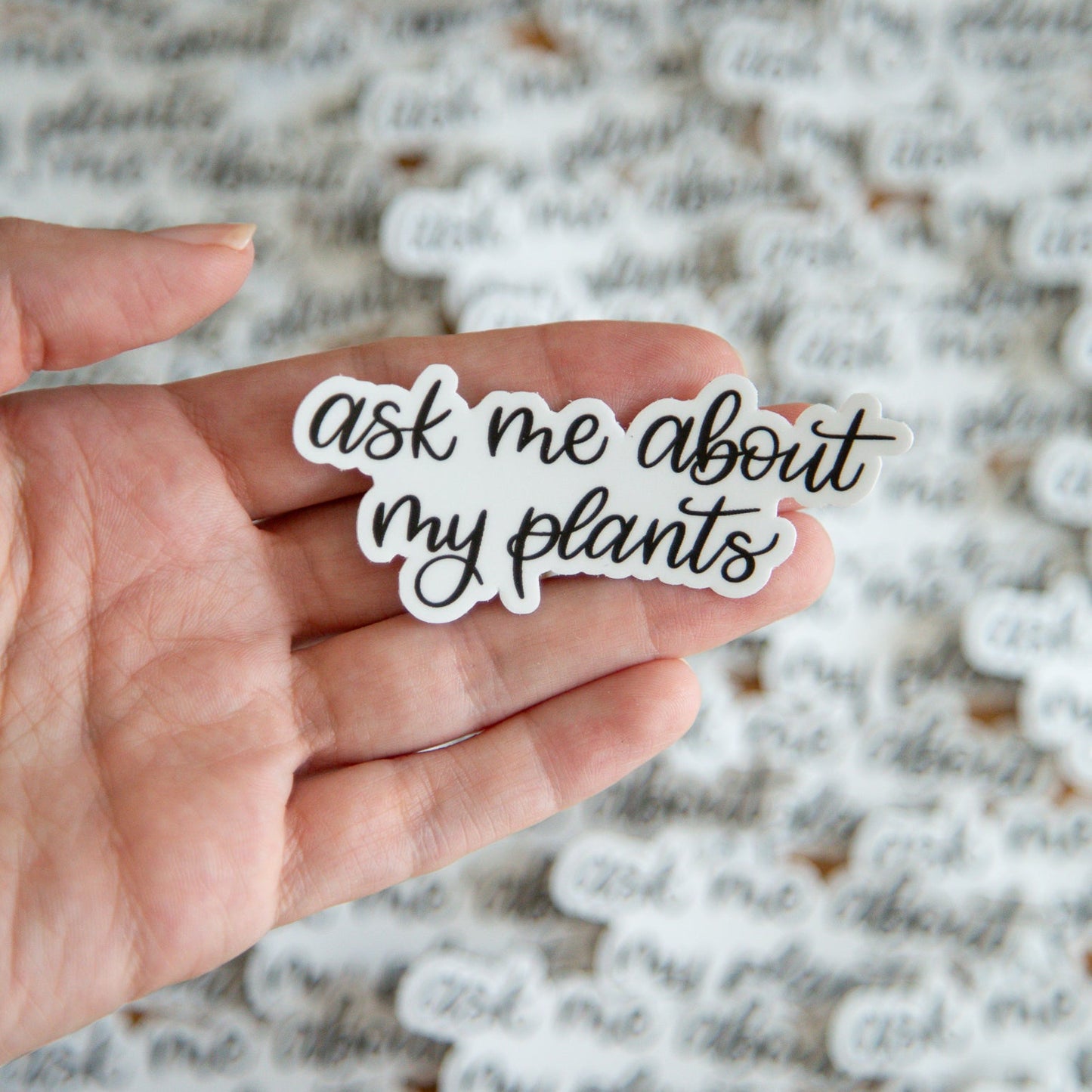 Hand holding a sticker with 'ask me about my plants' text against a textured background