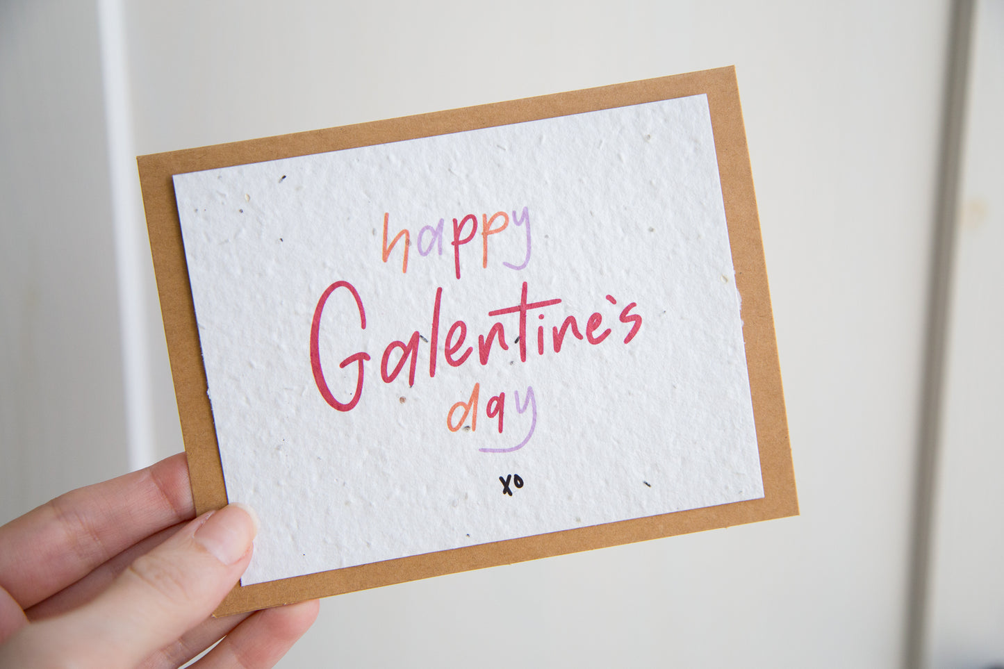 White greeting card with the words “happy Galentine’s Day xo” written in red orange and purple on plantable seed paper