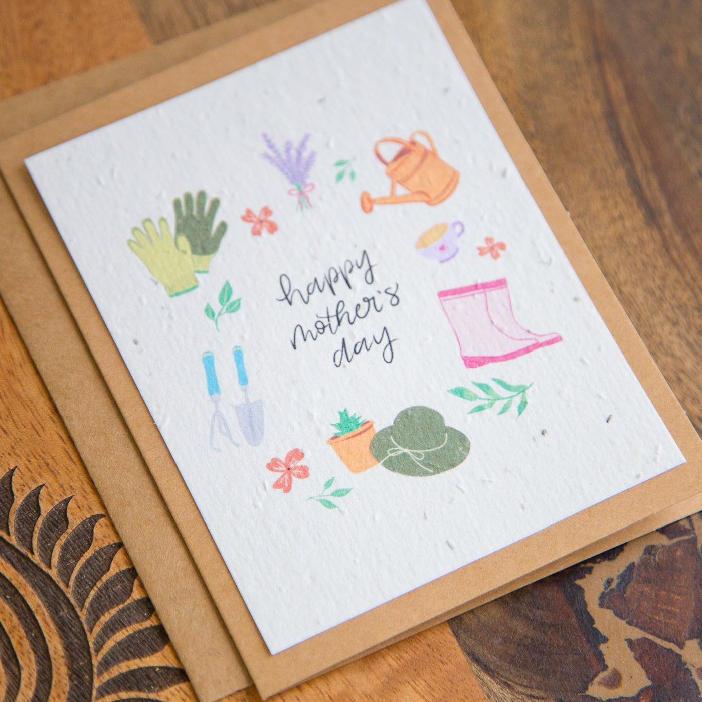 Greeting card with gardening-themed illustrations and 'Happy Mother's Day' text on a wooden surface.