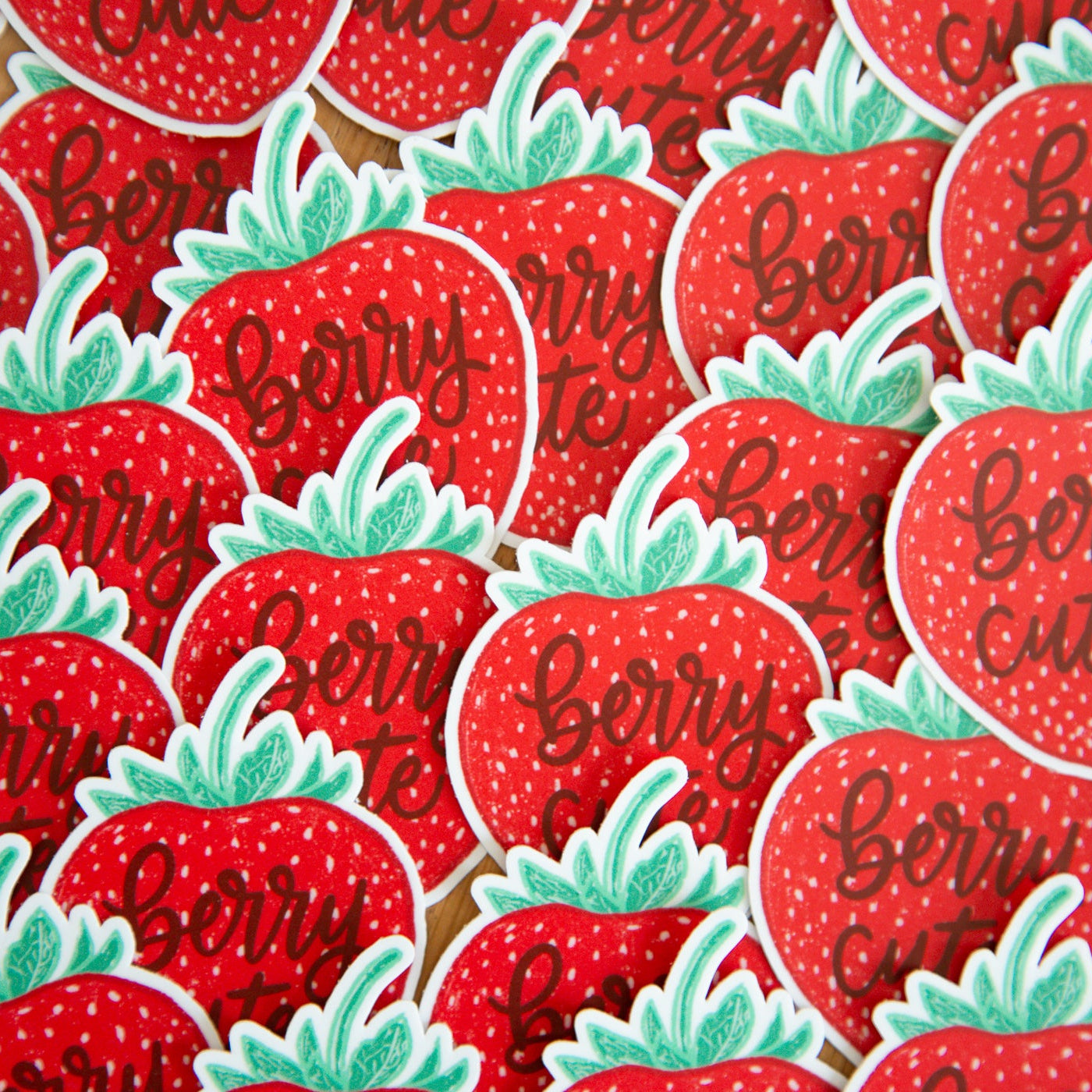Pattern of red strawberry stickers with green leaves and text that reads "berry cute" on a flat surface