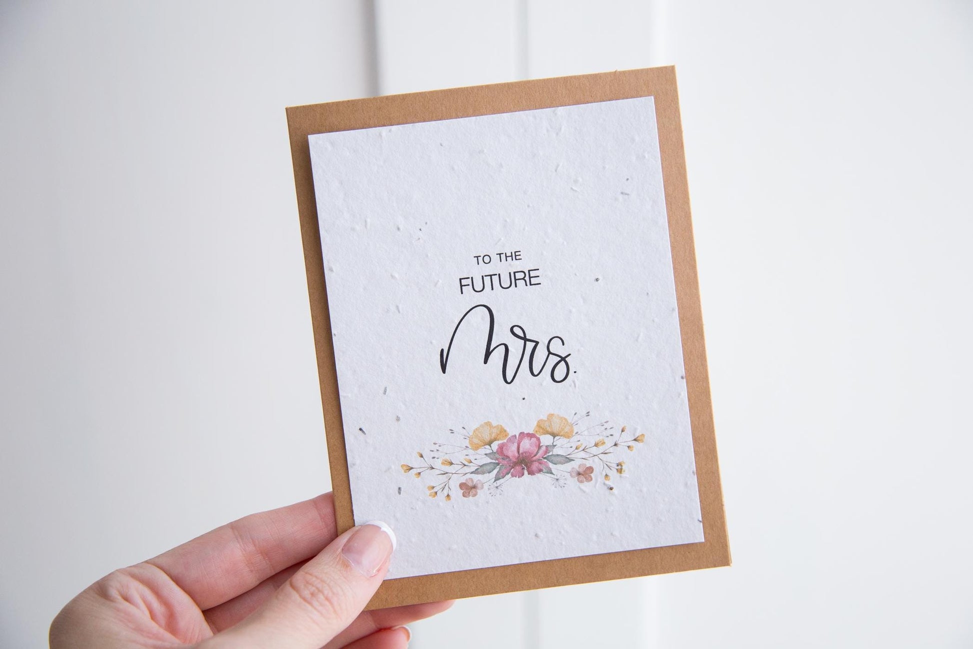 Hand holding a greeting card with the text "to the future Mrs." printed on white seed paper