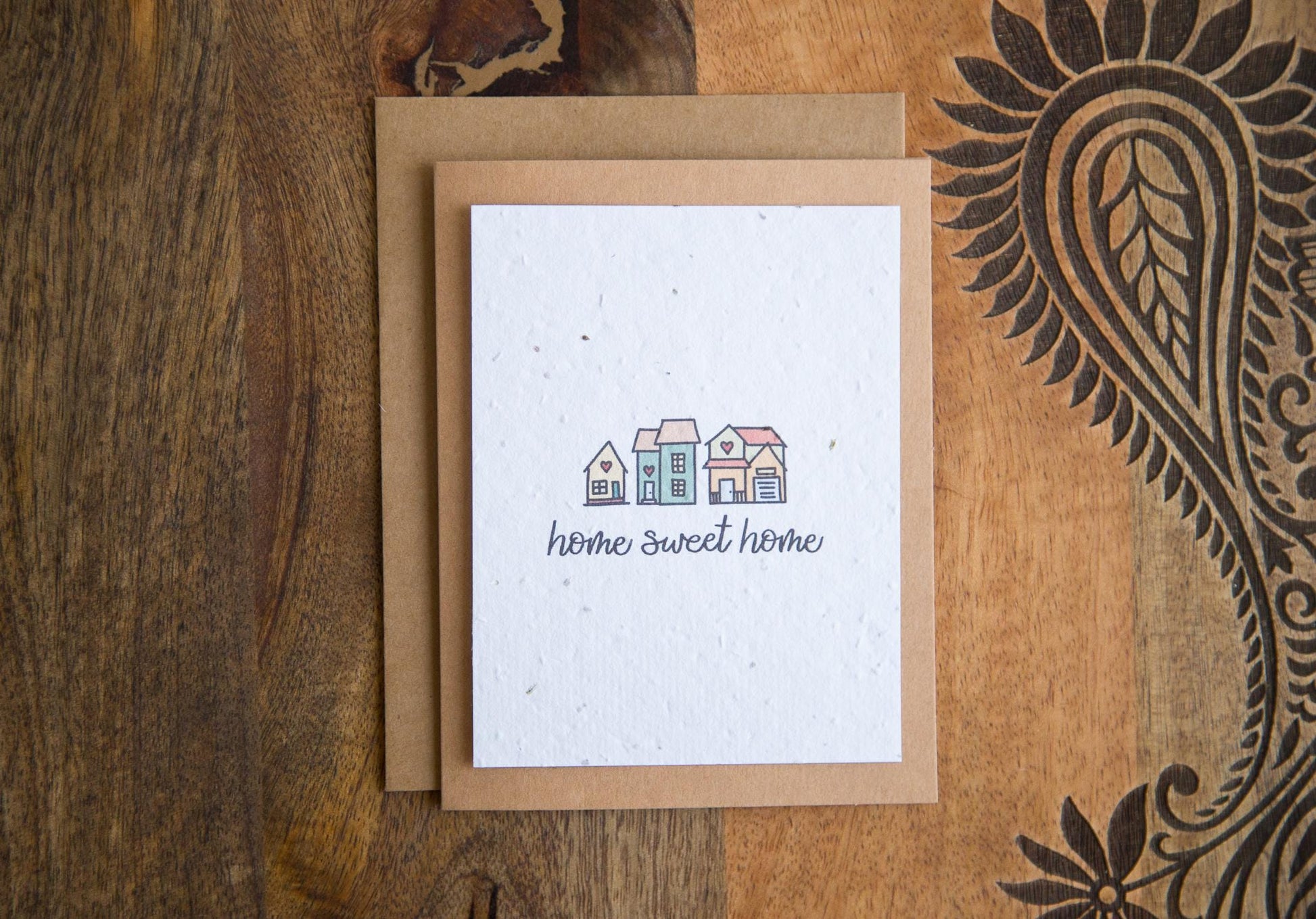 A2 greeting card on a table with the words "home sweet home" and an illustration of 3 small houses printed on white seed paper 