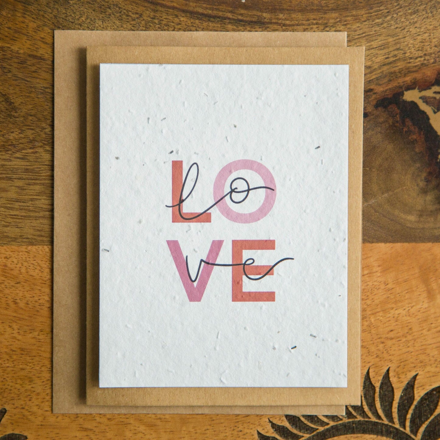 An A2 greeting card with the word LOVE in pink and red text print on white seed paper