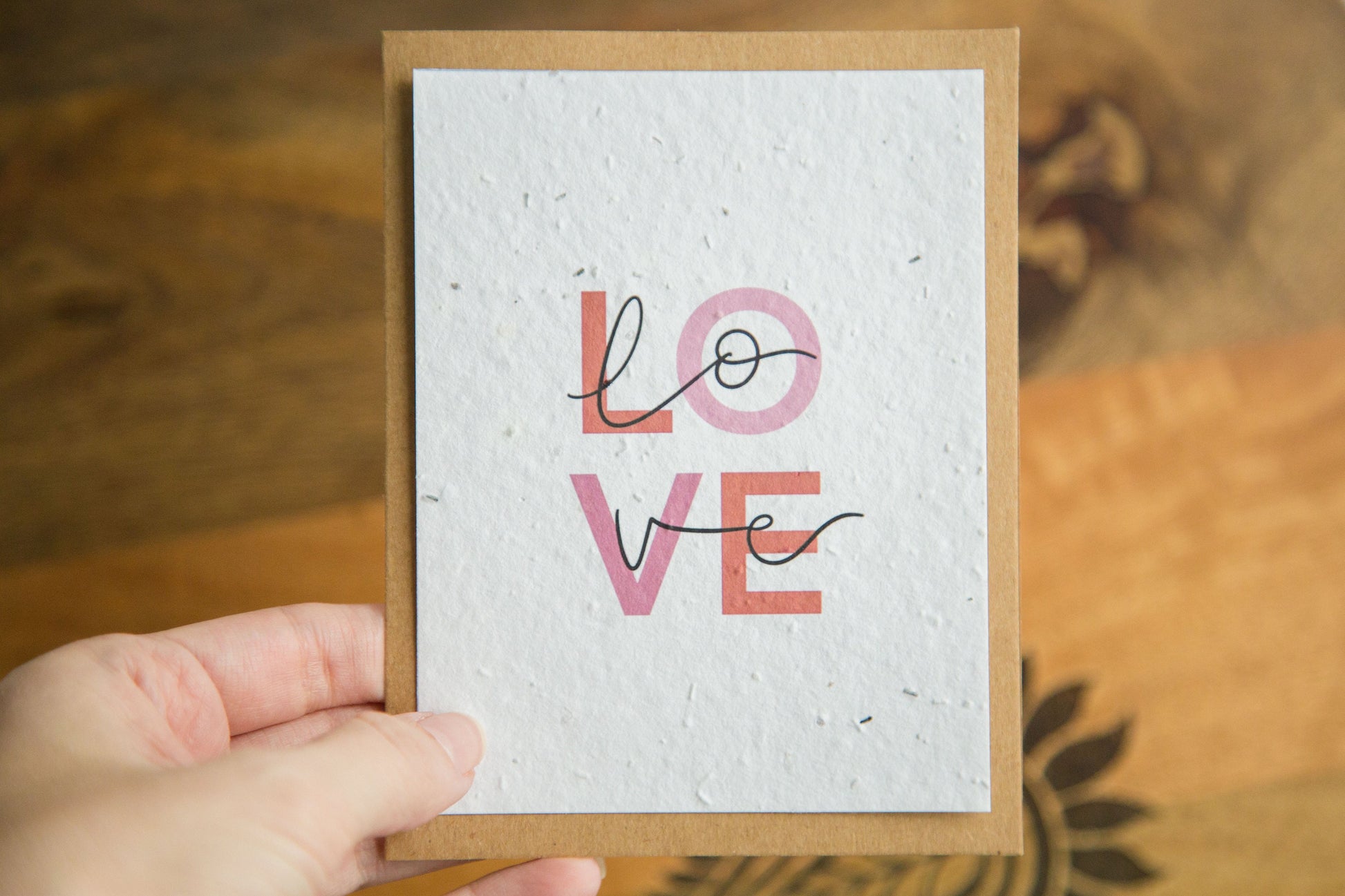 An A2 greeting card with the word LOVE in pink and red text print on white seed paper