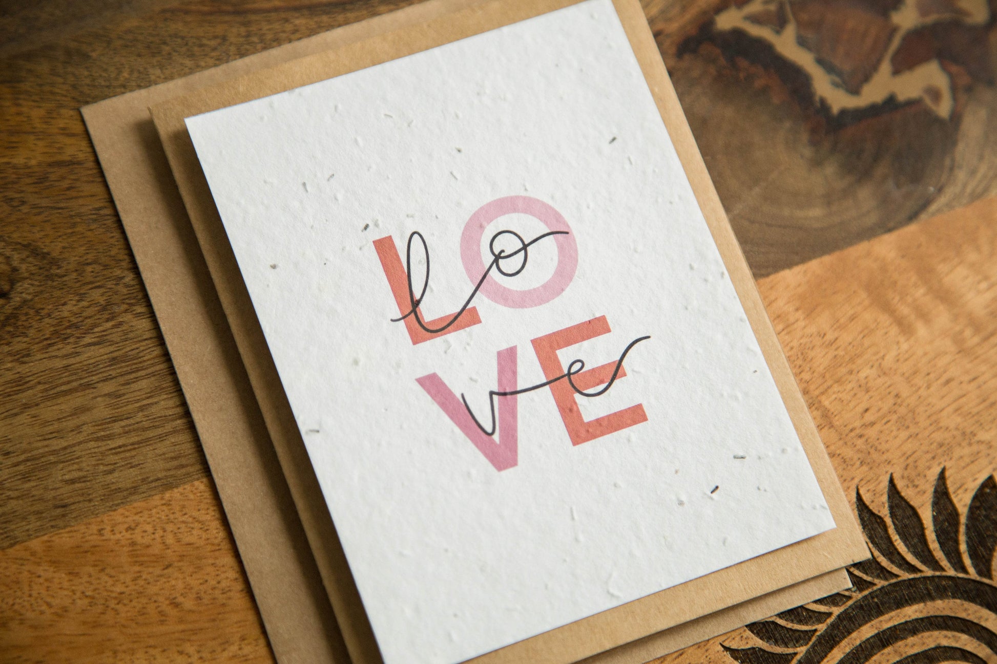 An A2 greeting card with the word LOVE in pink and red text print on white seed paper