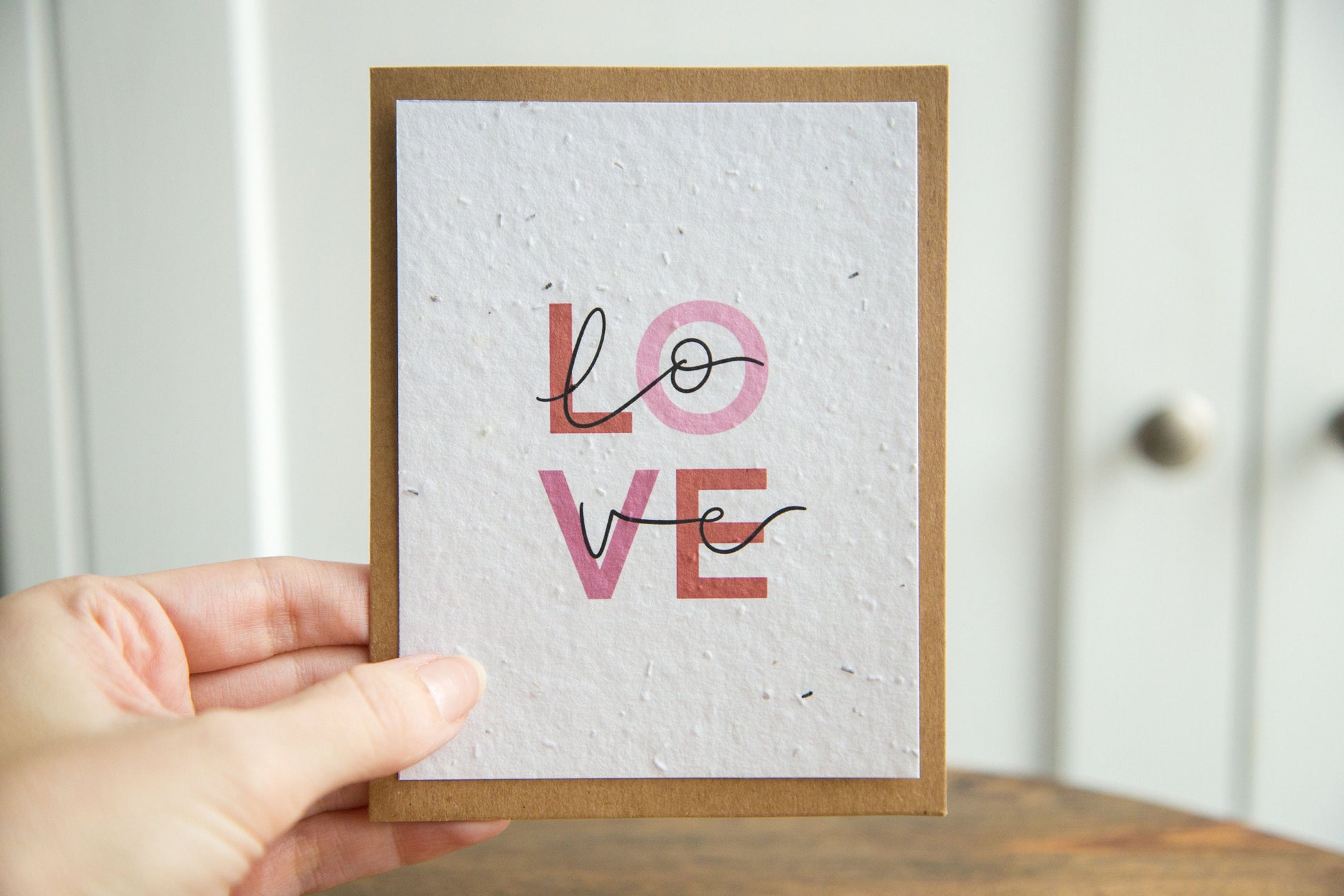 An A2 greeting card with the word LOVE in pink and red text print on white seed paper