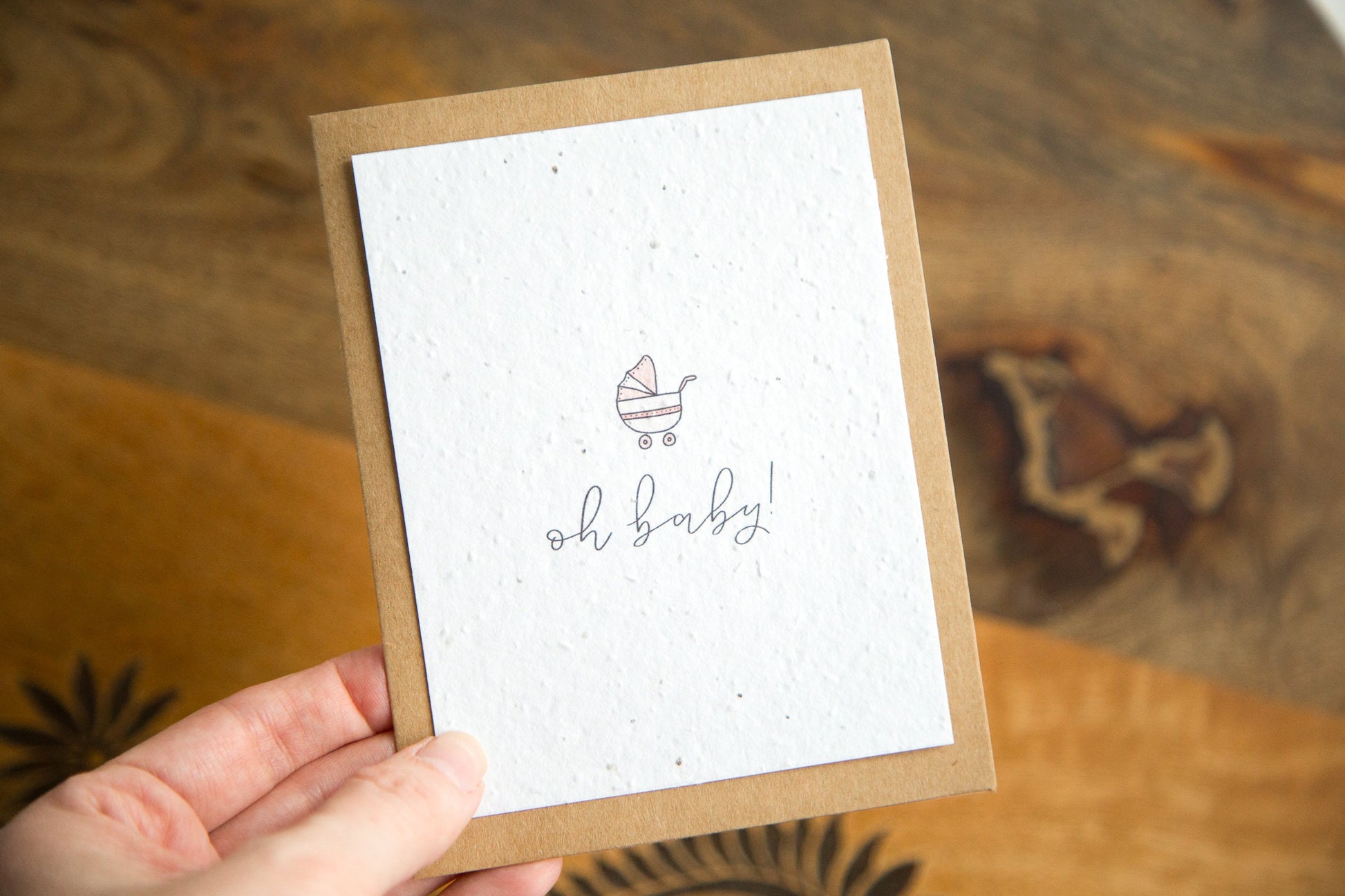 A2 greeting card with the word "oh baby!" and an illustration of a baby carriage in pink printed on white seed paper 
