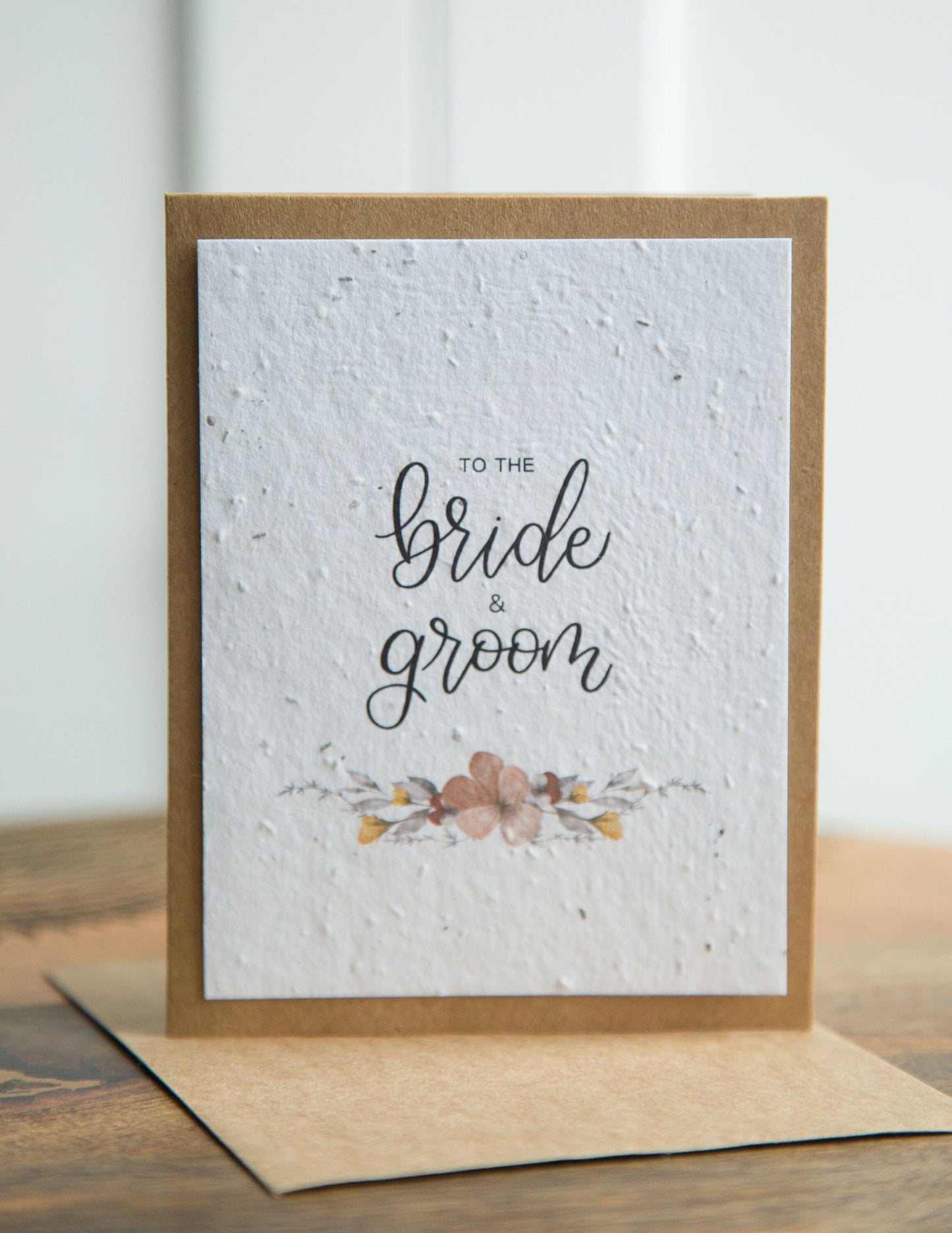 An A2 sized wedding card with floral designs and the text 'To the bride & groom' on the front, on white plantable seed paper